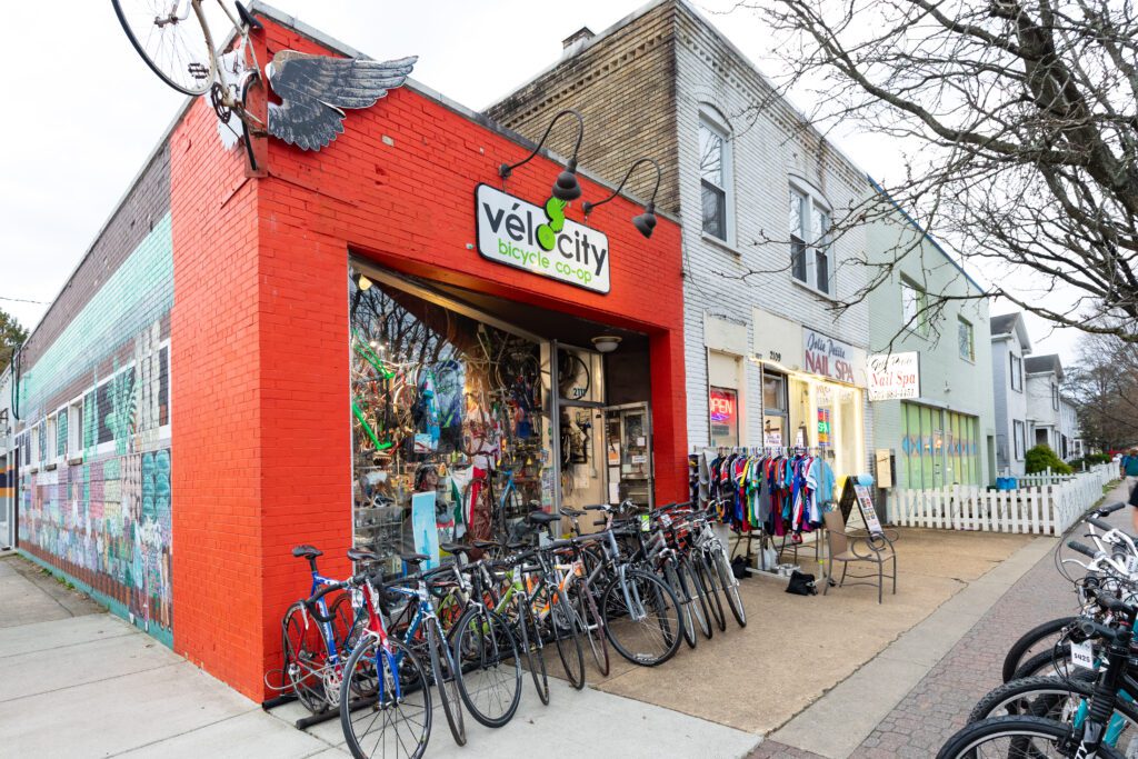 A photo of the velocity storefront in alexandria. It is a red brick building on the corner of a street. Dozens of bikes are lined up outside.